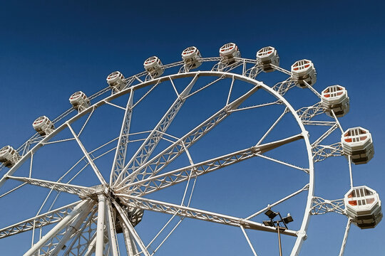 Barcelona, Spain - 05 December 2025: View of a large white Ferris wheel with passenger cabins against a clear blue sky.