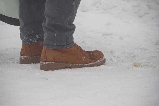 Person stands in snow wearing brown shoes near a snowy area
