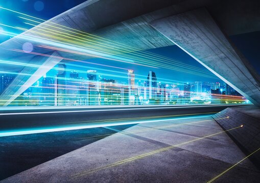 Long exposure night traffic under modern urban highway bridge with neon light trails