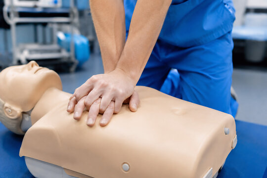 medical training photo showing only the hands of a healthcare professional performing chest compressions on a CPR training mannequin, emergency training room