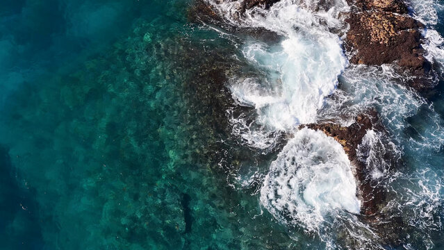 Aerial View of Turquoise Ocean Waves Crashing Against Dark Coastal Rocks