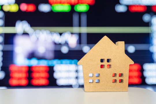Small wooden house model on table with stock market graph screen blur background, concept for real estate investment, home loan, interest rate, property mortgage, and insurance.