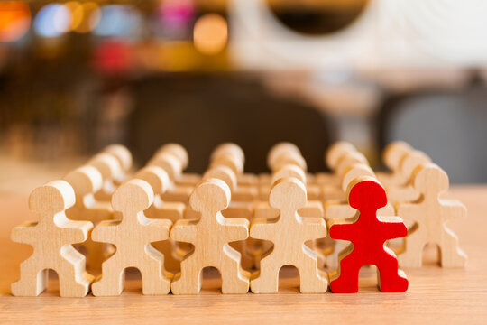 Unique red wooden figure standing out among natural wood people figures row, concept for leadership, uniqueness, individuality, recruitment, stand out, candidate, and distinction.