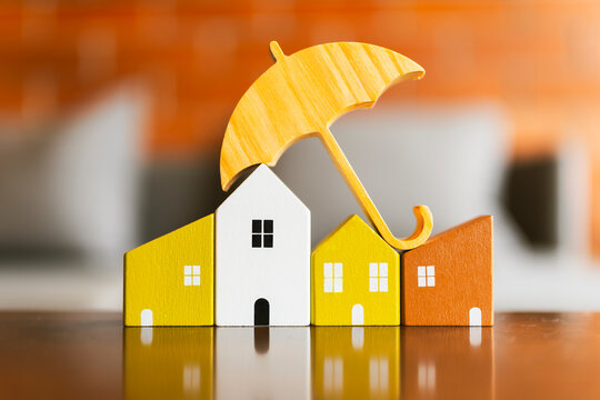 Small yellow wooden umbrella covering colorful house models, concept for real estate insurance, home protection, property loan security, family safety, and risk management.