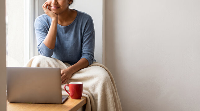 Woman smiling and working at laptop with coffee cup by window