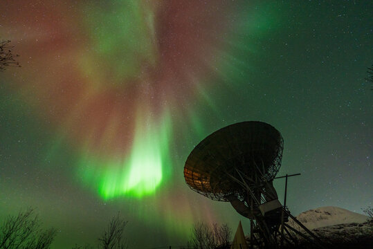 Ramfjordbotn, Troms, Norway - 07 October 2024: View of EISCAT Tromso radar dish illuminated by vibrant green and red aurora borealis in the night sky.