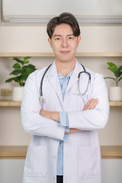 Asian male doctor wearing white coat with stethoscope arms crossed in clinic