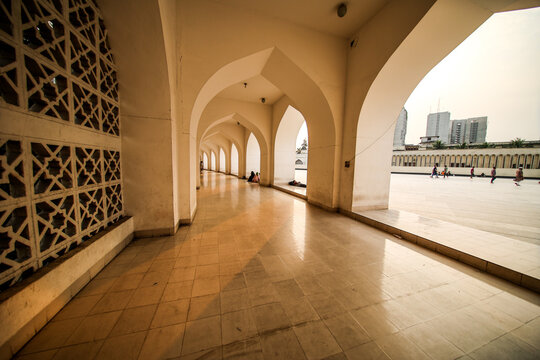 Dhaka, Dhaka Division, Bangladesh - 20 September 2024: View of the arched colonnade of the Baitul Mukarram National Mosque with people walking in the courtyard.
