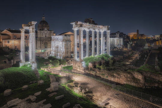 Roma, Italy - 07 November 2024: View of the illuminated ruins of the Imperial Fora at night, featuring ancient columns, the Arch of Septimius Severus, and historic stone architecture.