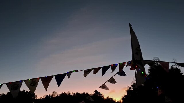 Colorful festive bunting flags and string lights flickering against dusk sky during outdoor evening celebration event.