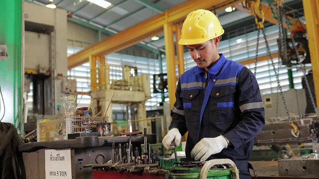 Professional factory engineer wearing a safety helmet and gloves inspects and assembles precision machinery parts on a modern industrial manufacturing production line.