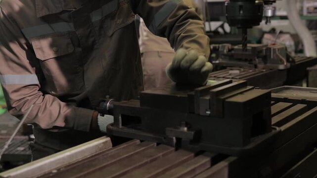 Close-up of a worker in protective uniform operating professional machinery and bench vice tool. Concepts of heavy industry, metal manufacturing, and precise engineering.