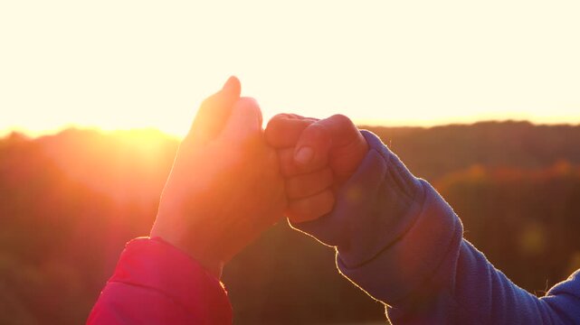 CLOSE UP, LENS FLARE: Adults making a fist bump against bright autumn sun. Authentic feeling of connection, support and shared success after hike in golden morning light above rolling countryside.