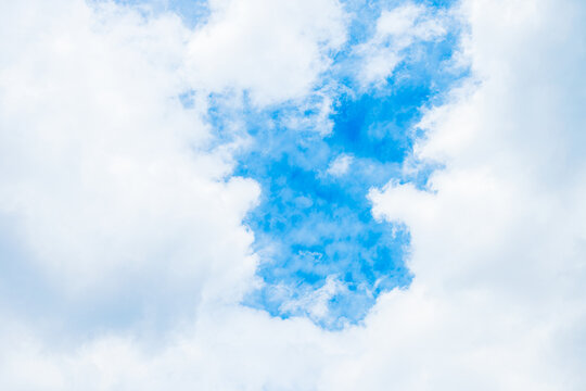 A clear patch of bright blue sky framed by soft, white fluffy clouds. Peaceful, natural atmosphere, high resolution, ideal for serene backgrounds