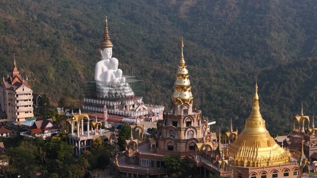 Aerial view flying around the five white Buddha statues at Wat Phra That Pha Son Kaew in Khao Kho, Thailand