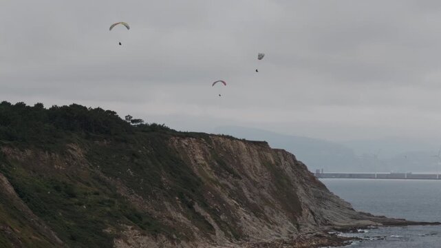 Three paragliders enjoying the coastal view and freedom while flying above ocean cliffs near a harbor