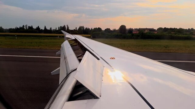 Airplane wing with spoilers extended viewed from passenger window. The aircraft is accelerating on the runway, preparing for takeoff at sunset