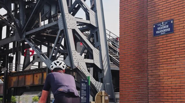 Cyclists riding past the industrial mechanism of the budabrug, a vertical-lift bridge over the brussels&ndash;scheldt maritime canal