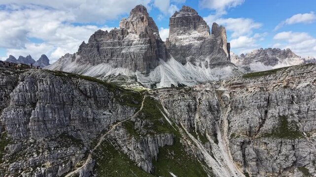Slow upward drone reveal of the iconic Tre Cime di Lavaredo emerging above rugged limestone cliffs in the Dolomites, Italy