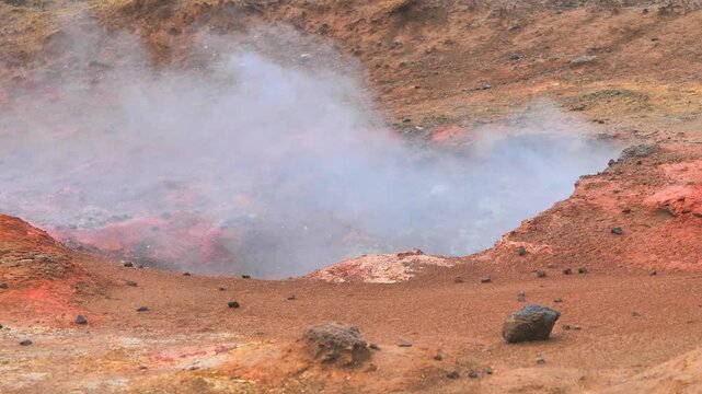 Static tripod footage of steaming geothermal mud pool at N&aacute;mafjall Hverir near Lake M&yacute;vatn, Iceland. Vibrant mineral colors, swirling steam, and rugged terrain in soft daylight.