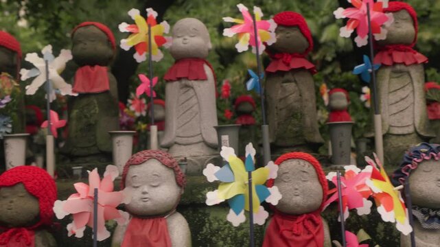 Stone Jizo Bosatsu Statues Wearing Knitted Caps And Bibs With Colorful Pinwheels And Flowers At Zojoji Temple In Tokyo, Japan. Tracking Shot