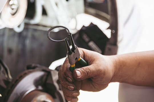 Close-up of a mechanic's hands holding circlip pliers to remove a retaining ring while repairing a car brake system in a workshop. Professional automotive maintenance and technical repair concept.