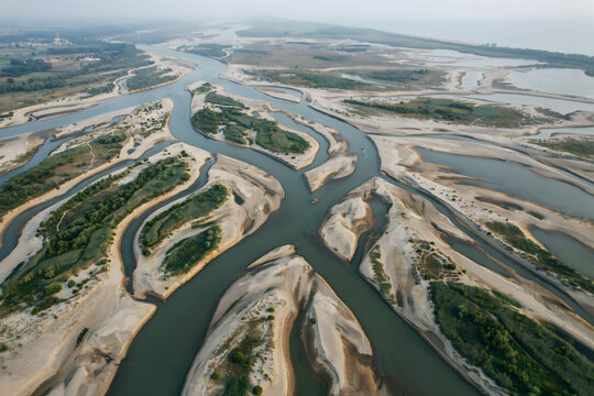 An aerial perspective of a wide river system featuring intricate sand islands and lush green patches, captured from above during a hazy daytime