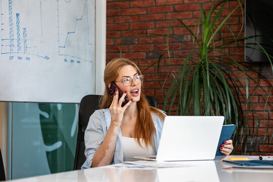 Business communication. Office phone call, Woman talking on mobile phone at desk, Corporate and work concept. Focused female manager calling with smartphone while working on laptop and notebook.