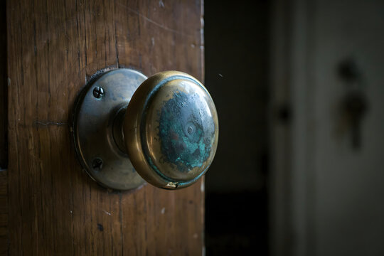 Close up of a vintage brass door knob with a weathered teal glass center attached to an old wooden door with visible wood grain texture