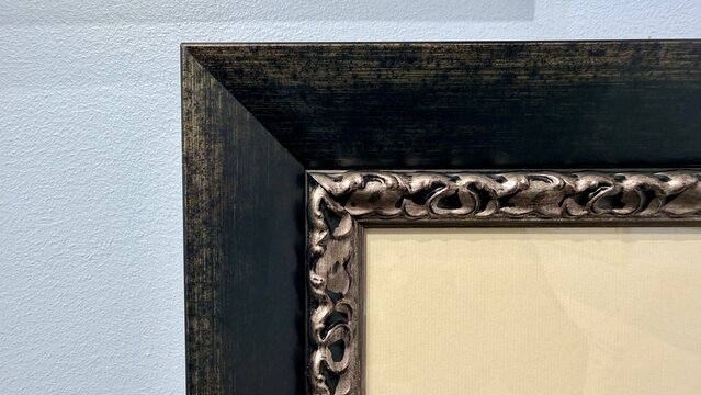 Close up of a classic picture frame corner with ornate vintage design and dark wooden border. Elegant framing moulding details on a textured white gallery wall. Art presentation mock up.