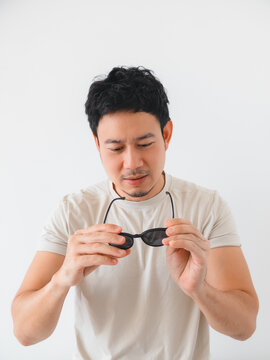 Young Asian man holding black sunglasses, examining them against a clean white background