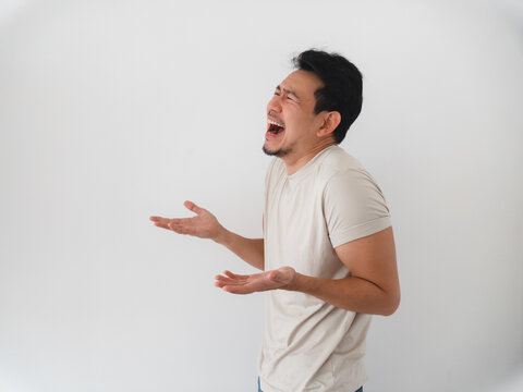 Joyful Asian man laughing loudly with wide open mouth and expressive hands on white background