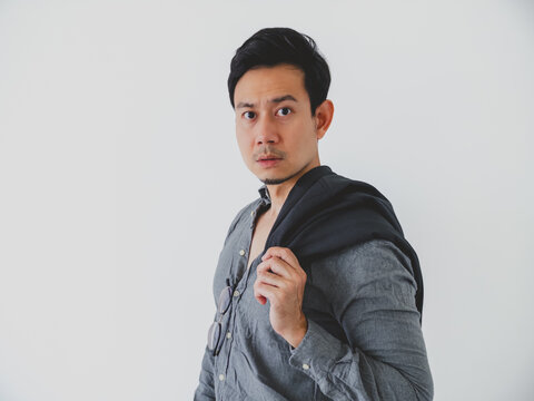 Serious young Asian man in grey shirt, jacket over shoulder, looking at camera.