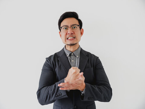 Young Asian businessman in a suit clenches his hands, expressing intense frustration and determination.
