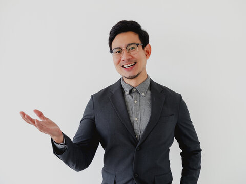 Smiling young Asian man in suit and glasses, presenting with an open hand.