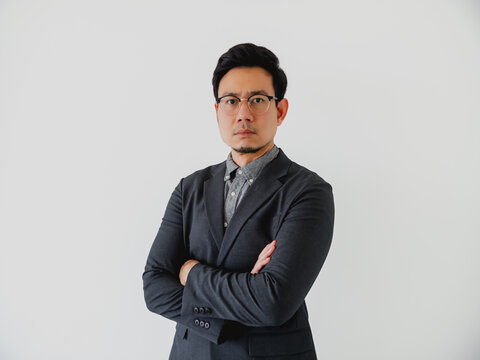 Serious Asian businessman in a dark suit and glasses standing with arms crossed.
