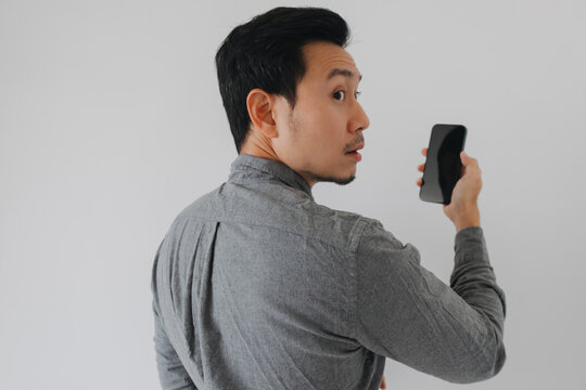 Young Asian man turns back with a surprised expression, holding a smartphone.