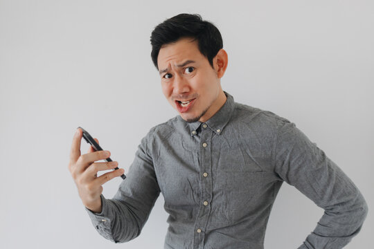Confused Asian Man Holding a Smartphone with a Frustrated Expression Looking at the Camera