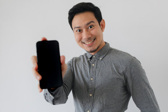 Cheerful Asian man holding up a smartphone with a blank screen for your content.