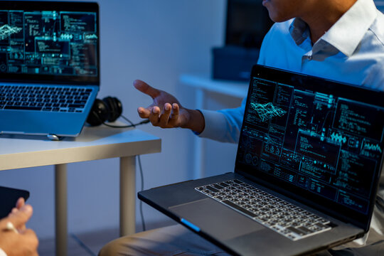 Two professionals discussing data analysis and cybersecurity on laptops with glowing dashboard screens in a modern office