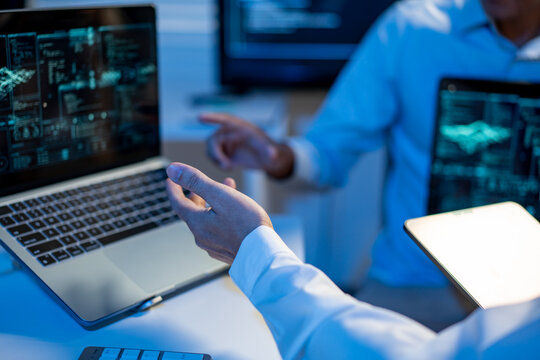 Two professionals discussing code on laptops in a blue lit office