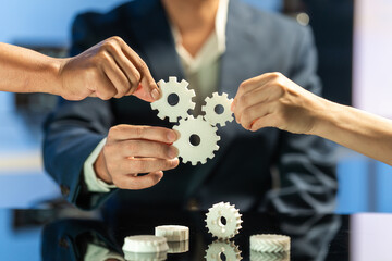 Fototapeta premium Hands fitting three gear puzzle pieces together in a business setting, showing teamwork, planning, and cooperation