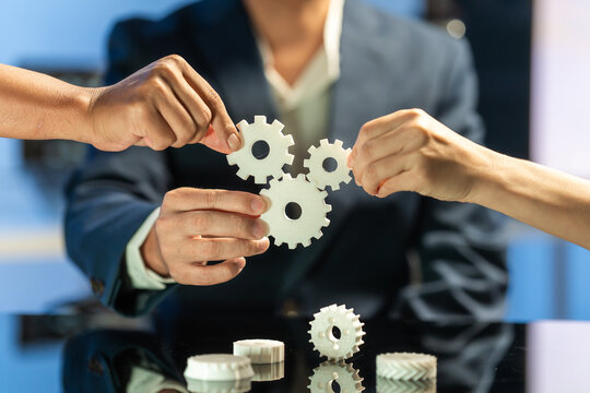 Hands fitting three gear puzzle pieces together in a business setting, showing teamwork, planning, and cooperation