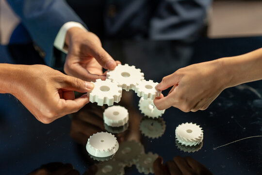 Hands of business people assembling white gears on a table, showing teamwork, cooperation and problem solving.
