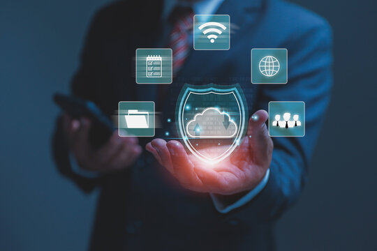 A businessman holds a glowing shield icon representing secure cloud data storage. Smart cybersecurity tools keep files safe from internet dangers.