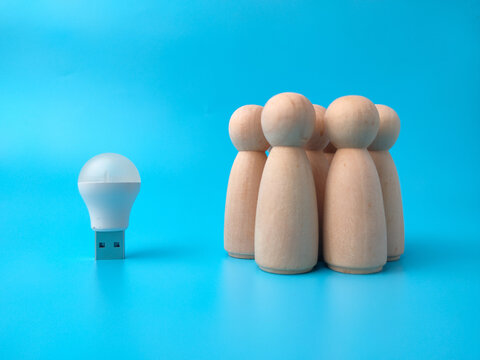 A small USB light bulb sits next to a group of wooden peg figures on a blue background
