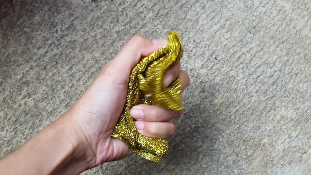 Close-up video of a hand squeezing a dry gold metallic kitchen scrubber sponge. Household cleaning tool demonstration with natural movement, suitable for cleaning, kitchen, and product advertising