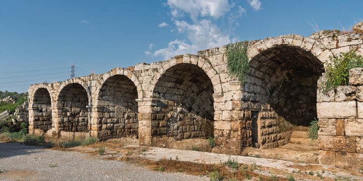 Stone arches of the ancient Roman Stadium at the archaeological site of Perge in Antalya, Turkey, showing the exterior wall architecture under a bright blue sky