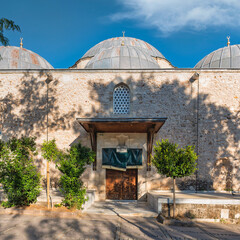 Fototapeta premium Exterior view of the historic Tekeli Mehmet Pasa Mosque featuring stone masonry and lead-covered domes in the old town district of Antalya, Turkey