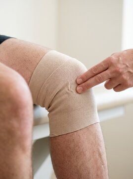 Doctor examining a patient knee wrapped in elastic compression bandage